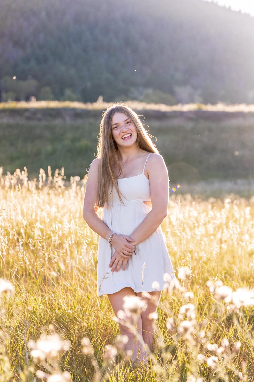 High school senior in a white dress standing in the golden meadow at Elk Meadow Park, Evergreen