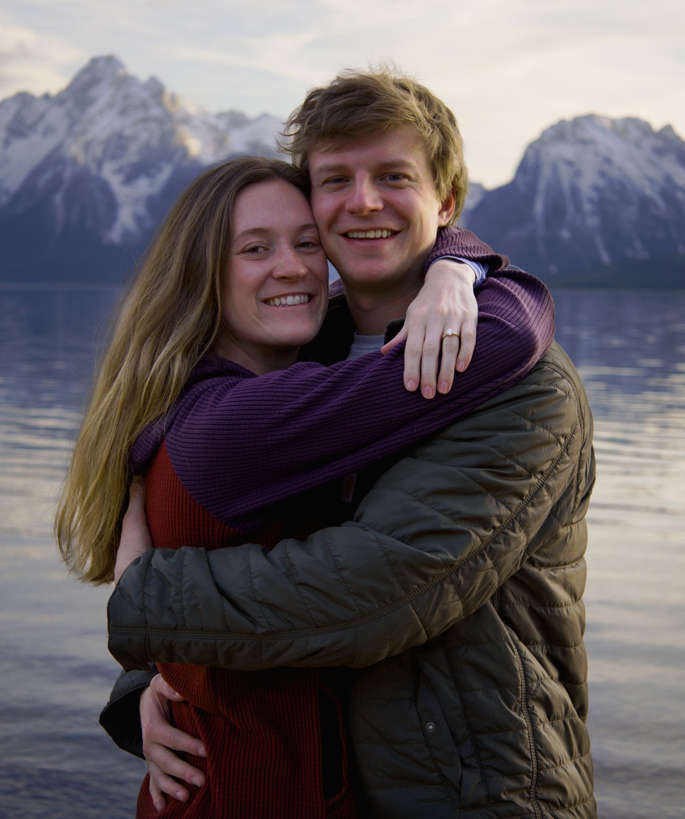 Engaged couple hugging and smiling on the lakeshore with the Teton Range behind them, Grand Teton National Park