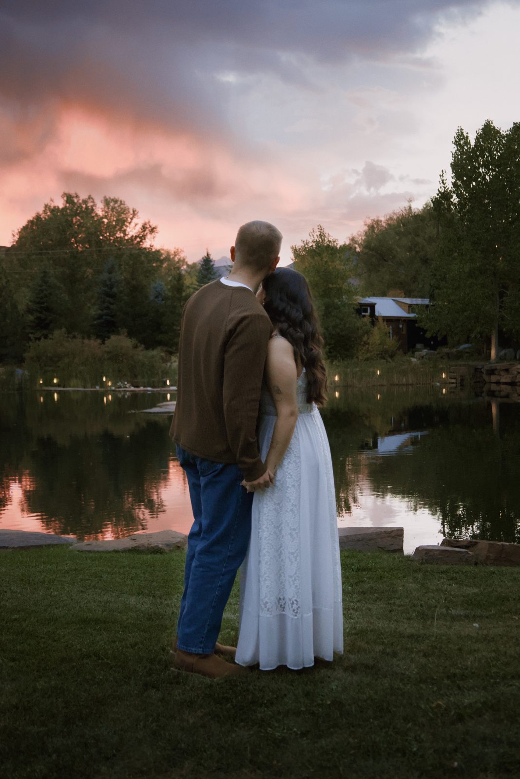 Couple holding each other by the pond at Lazy Stud Ranch under a pink sky after sunset