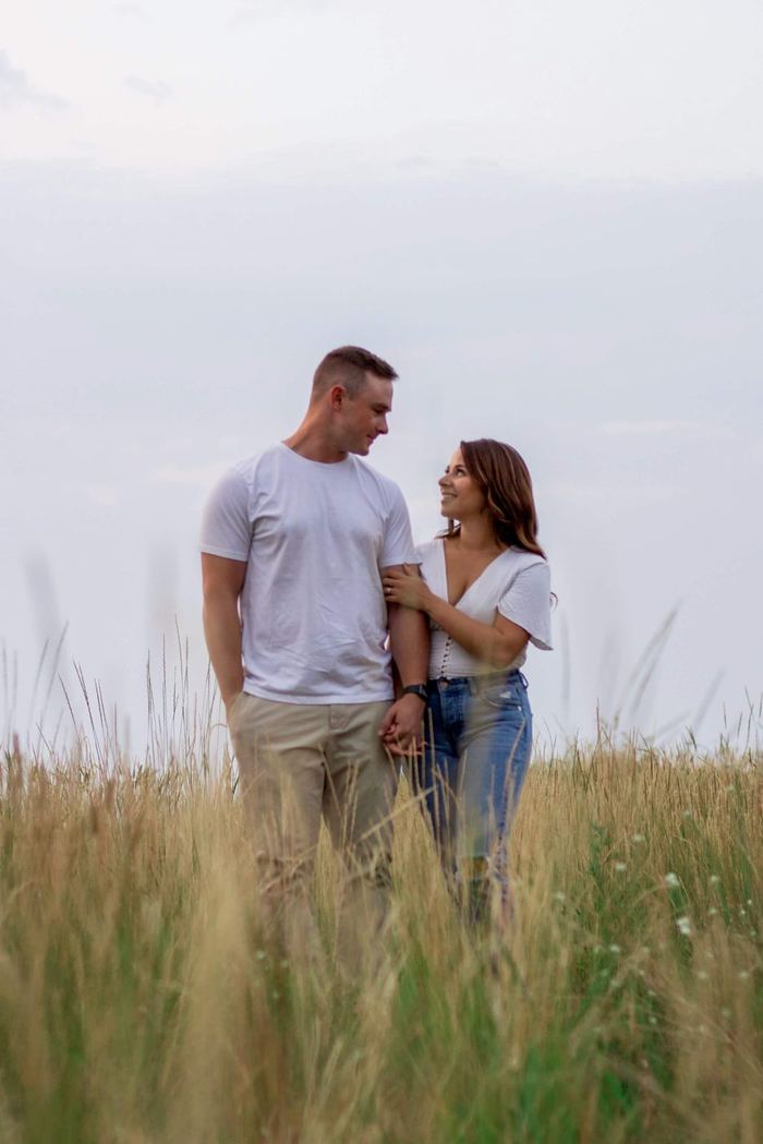 Newly engaged couple standing close in the tall grass at golden hour, Castle Rock