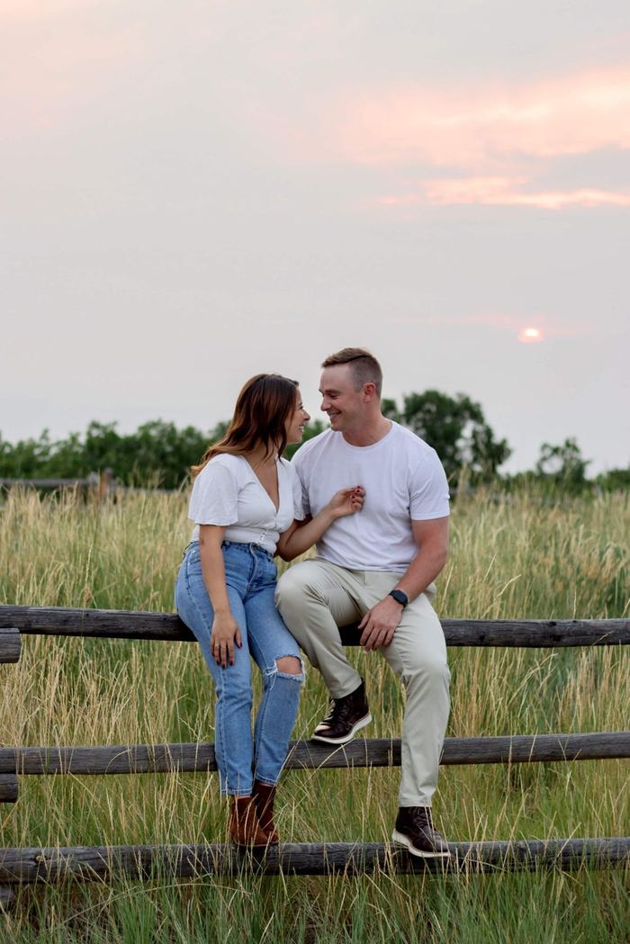 Couple laughing together on the rail fence at sunset