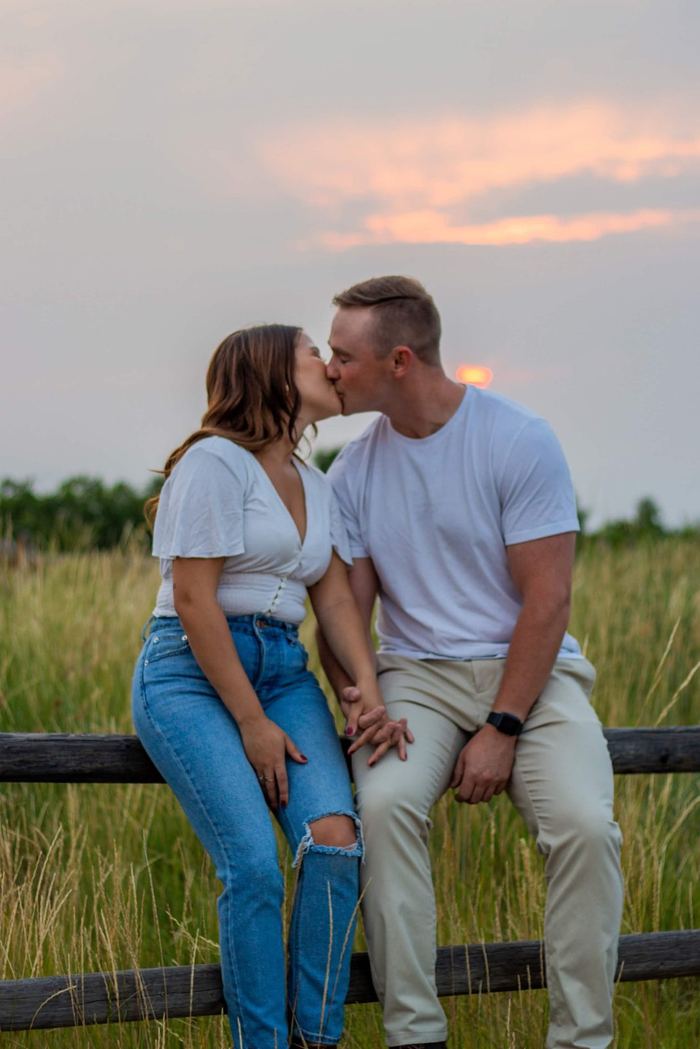 Kiss on the fence with a pink sunset sky behind them