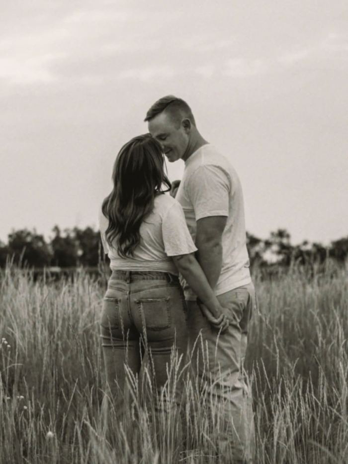 Black and white photo of the couple embracing in the tall grass