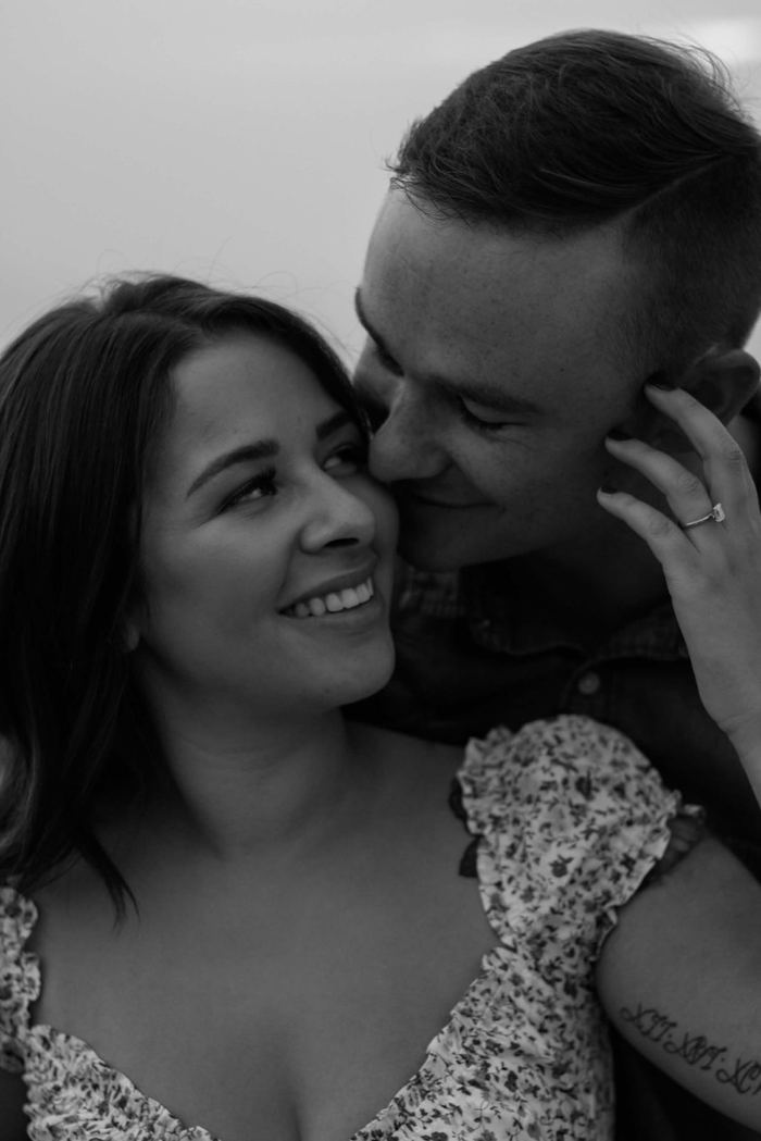 Black and white close-up of the couple smiling cheek to cheek, ring in view