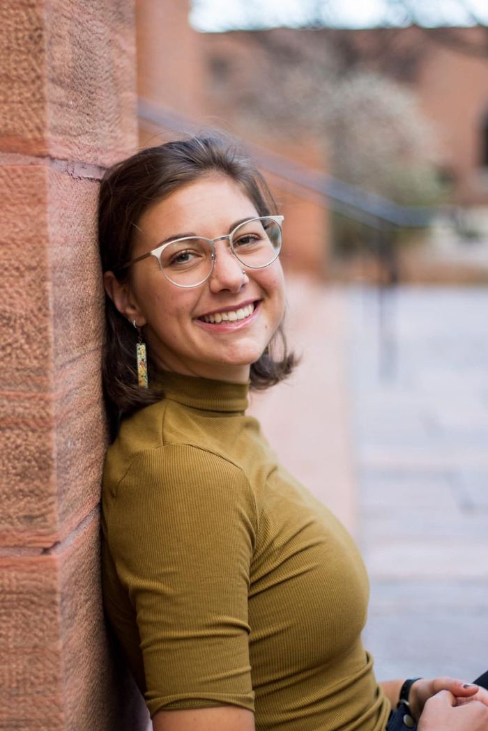 Senior leaning against a red sandstone wall, smiling at the camera