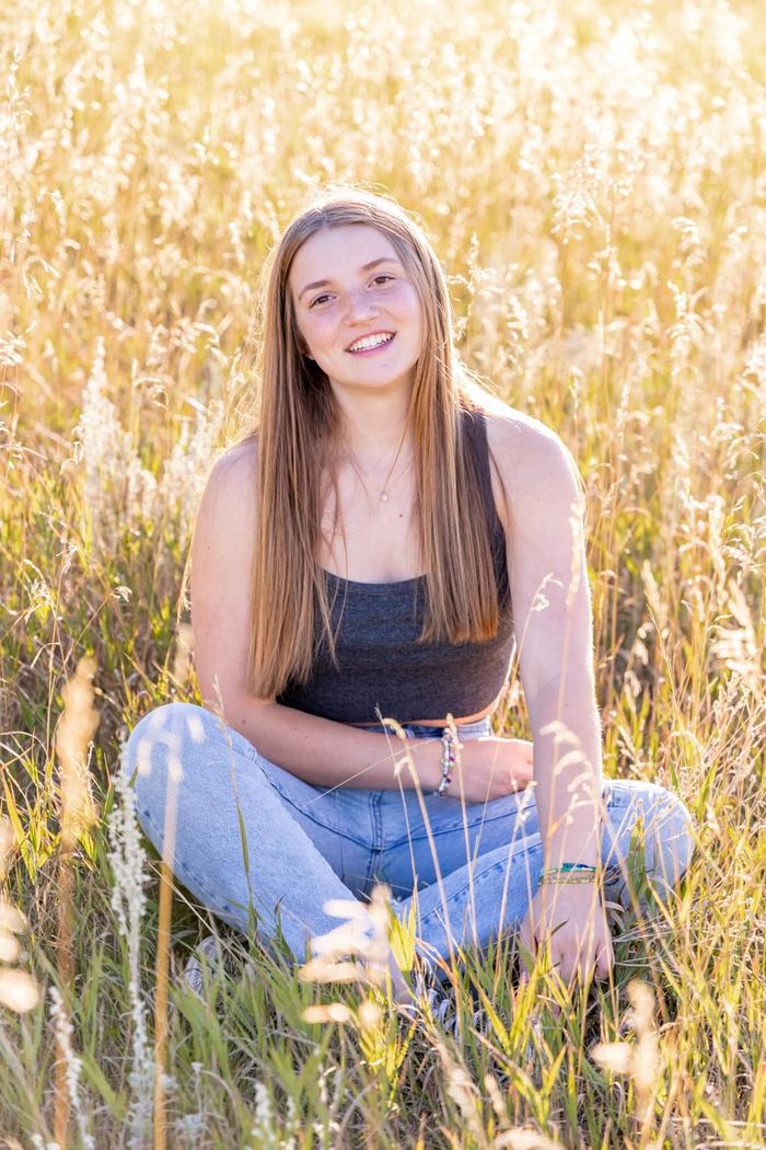 Senior sitting in the tall golden grass, smiling at the camera