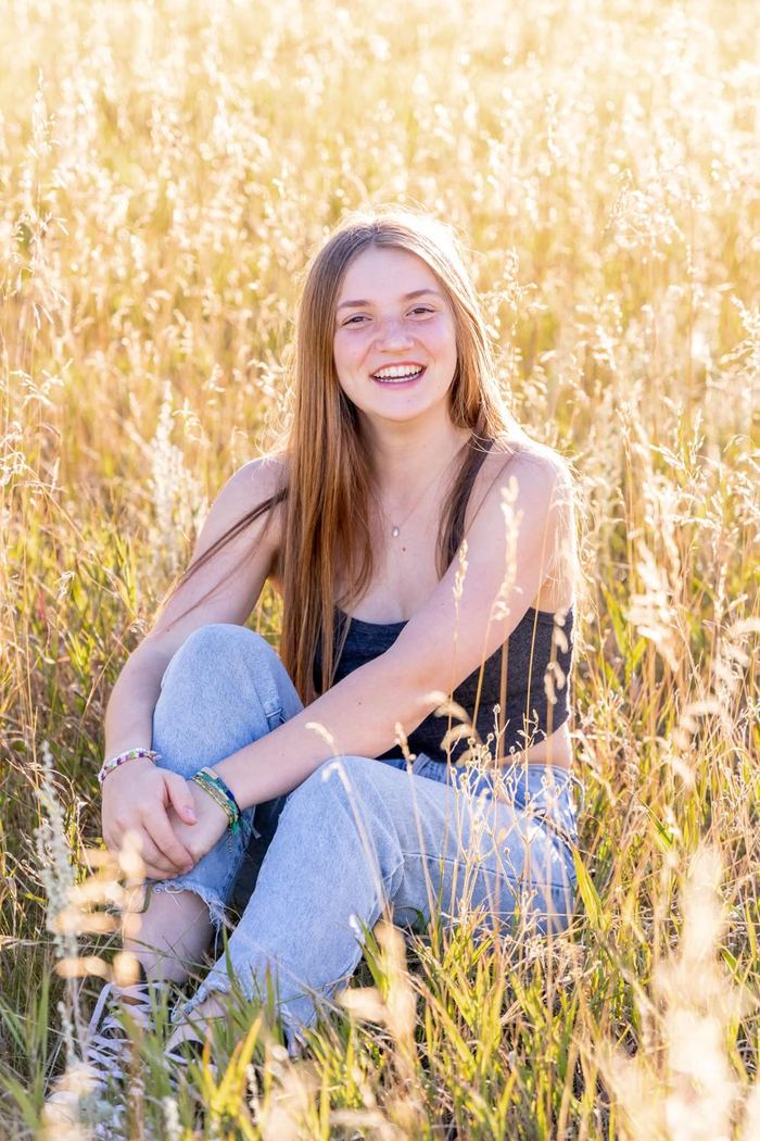 Senior sitting in the tall golden grass with her arms around her knees at Elk Meadow Park
