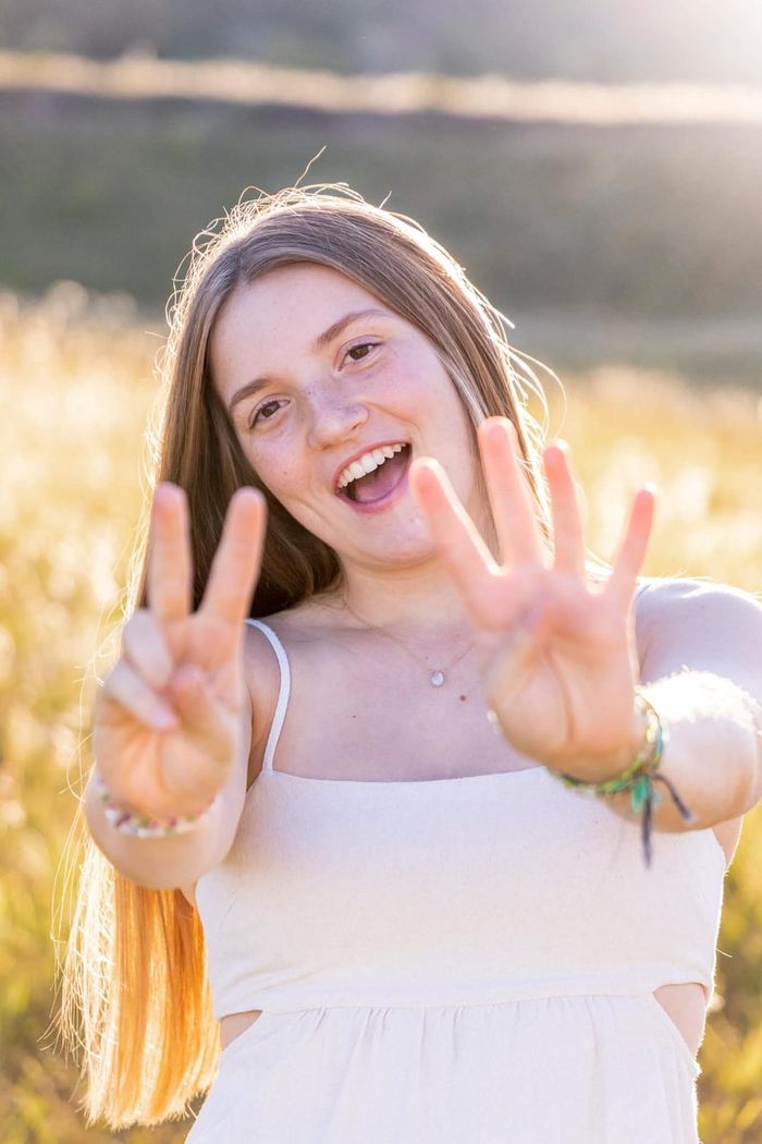 Senior smiling and holding up peace signs in the golden light