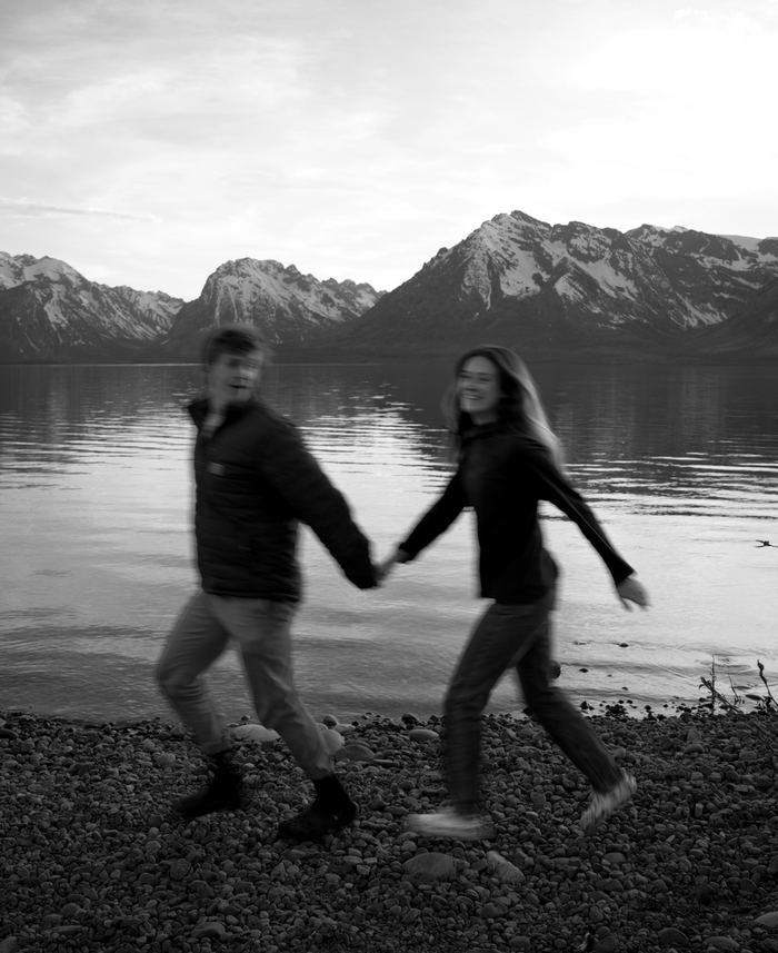 Black and white photo of the couple walking hand in hand along the rocky lakeshore in Grand Teton