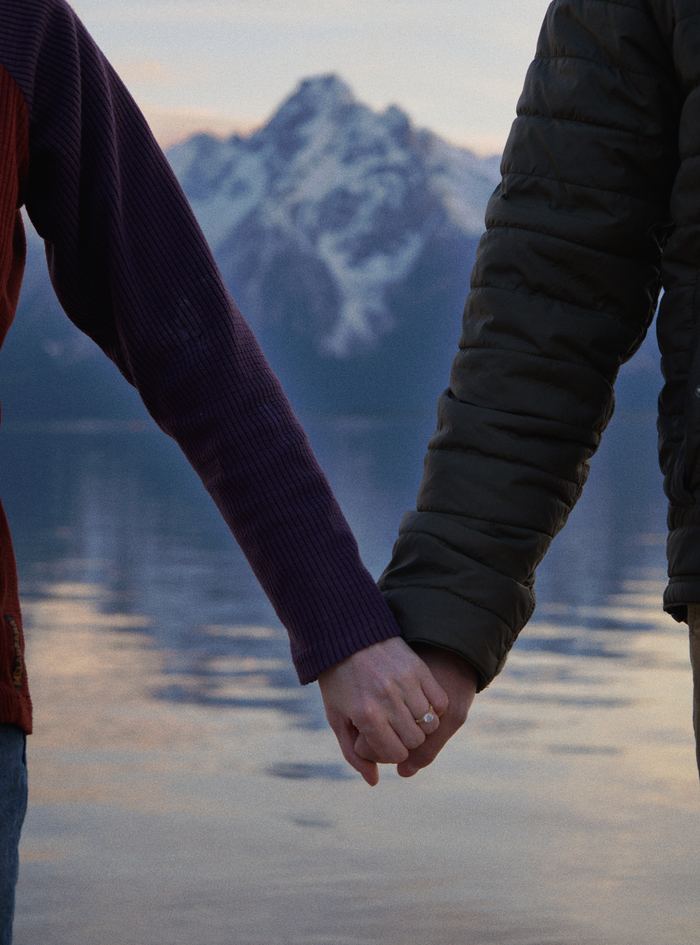 Close-up of the couple holding hands with the lake and snowy Teton peaks between them