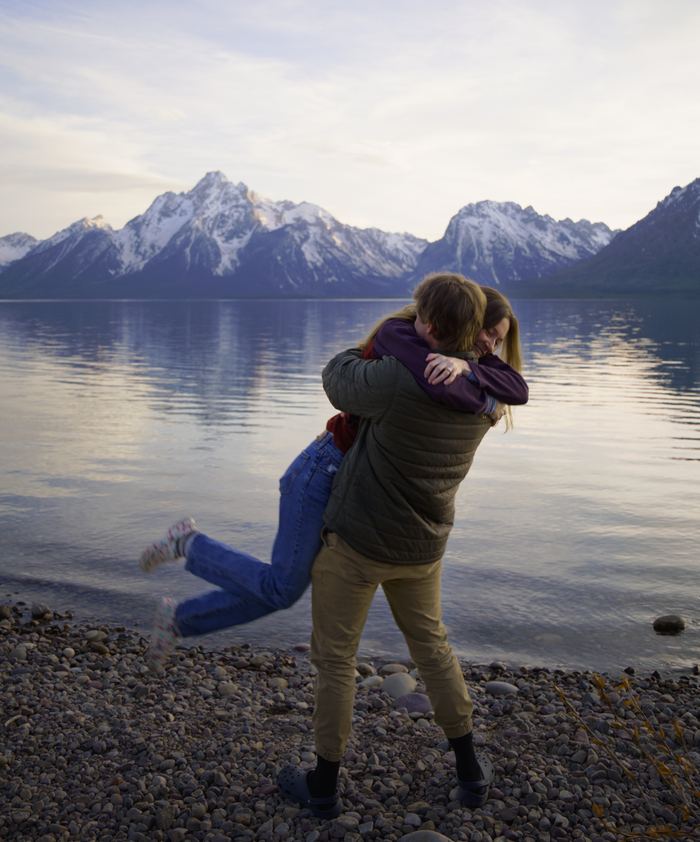 She jumps into his arms for a hug on the lakeshore in Grand Teton National Park