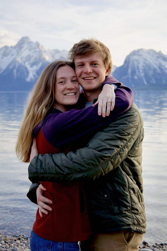 Engaged couple hugging and smiling on the lakeshore with the Teton Range behind them, Grand Teton National Park