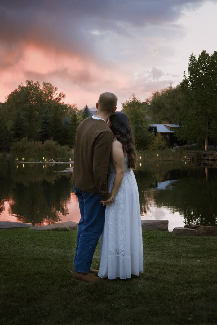 Couple holding each other by the pond at Lazy Stud Ranch under a pink sky after sunset