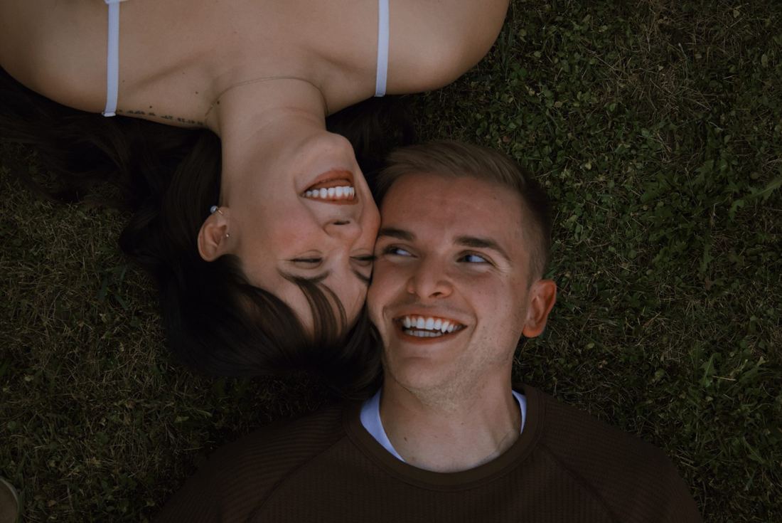 Couple lying in the grass head to head, both laughing