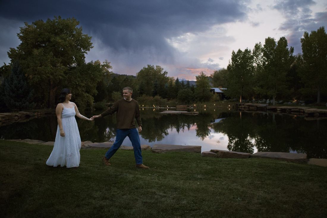 She leads him by the hand across the lawn by the pond during blue hour