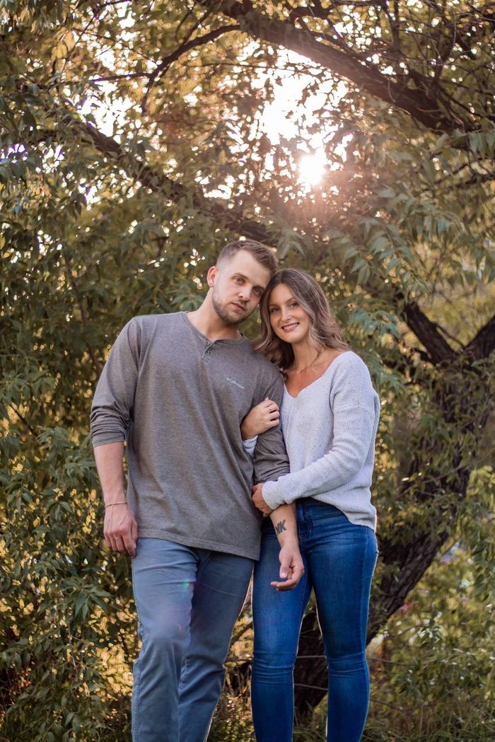 Couple standing close under a big tree with sunlight shining through the leaves in Washington Park, Denver