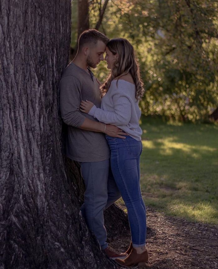 Couple leaning against a large tree trunk with their faces close together in Wash Park