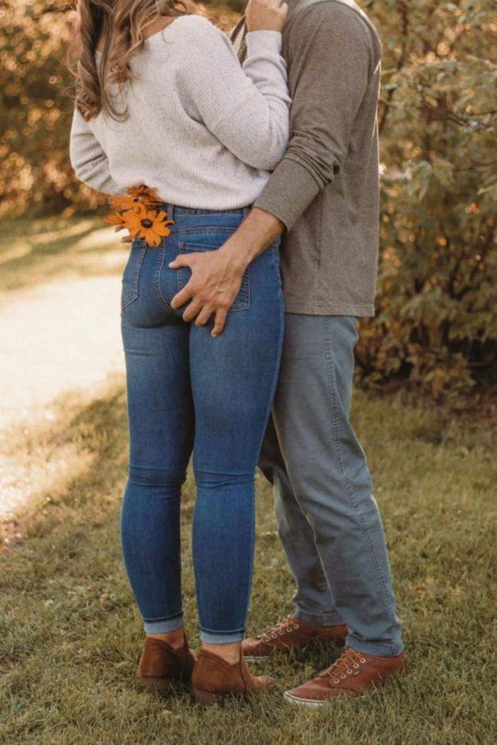 View from behind of a couple embracing, with an orange flower tucked in her back jeans pocket