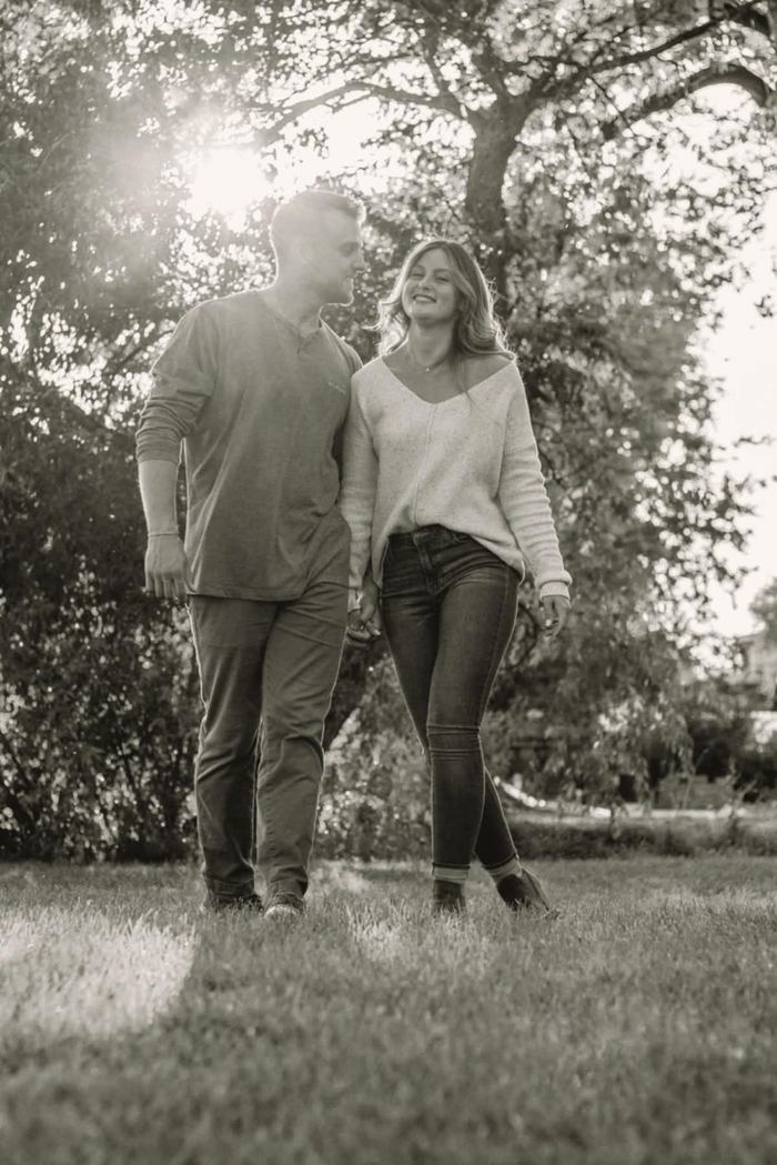 Black and white photo of a couple walking together through the trees in Wash Park
