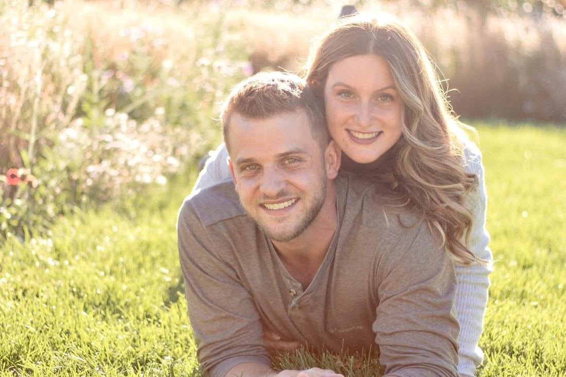 Close-up of the couple lying in the grass, her arms around his shoulders, both smiling