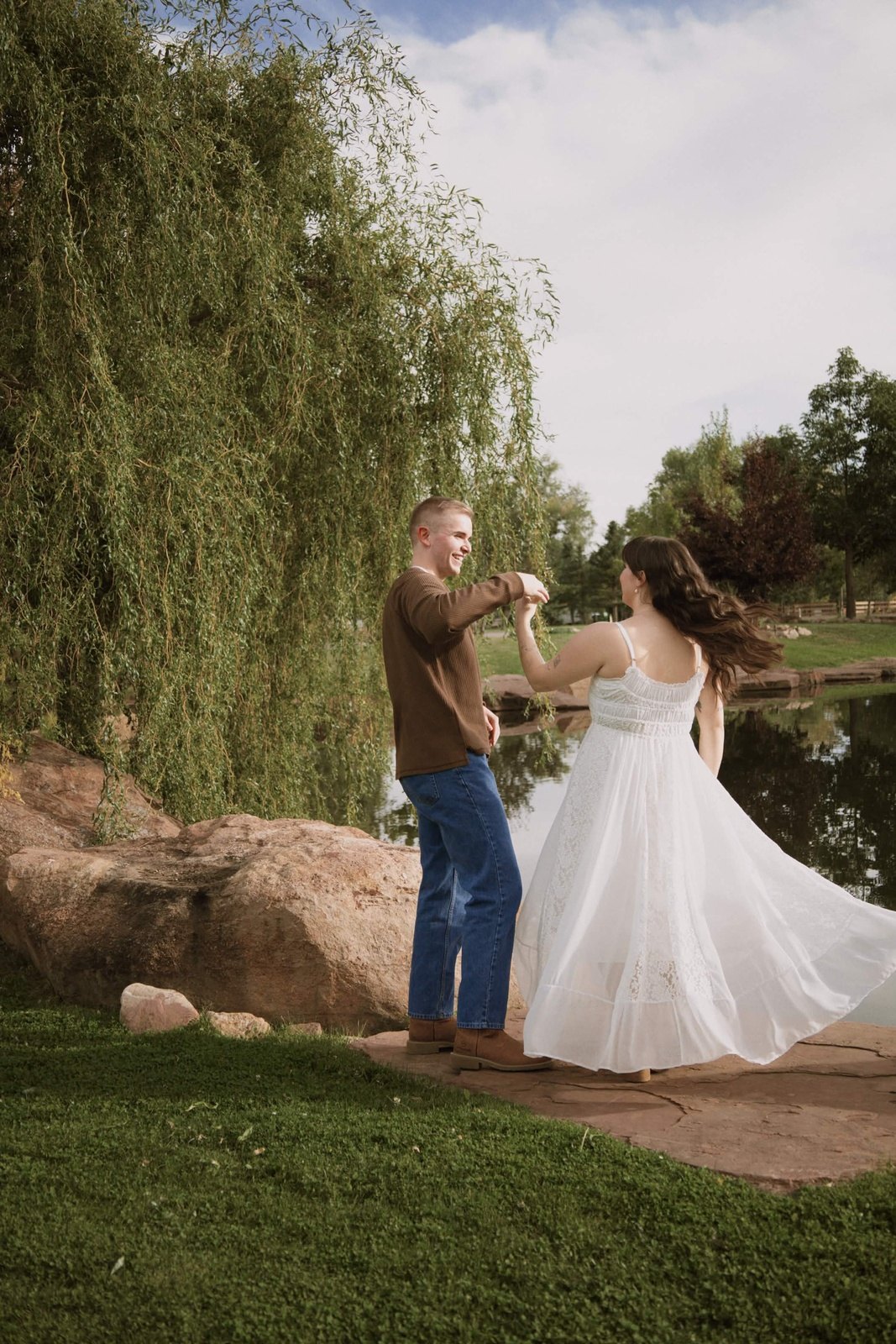 Couple twirling under willow trees by a pond