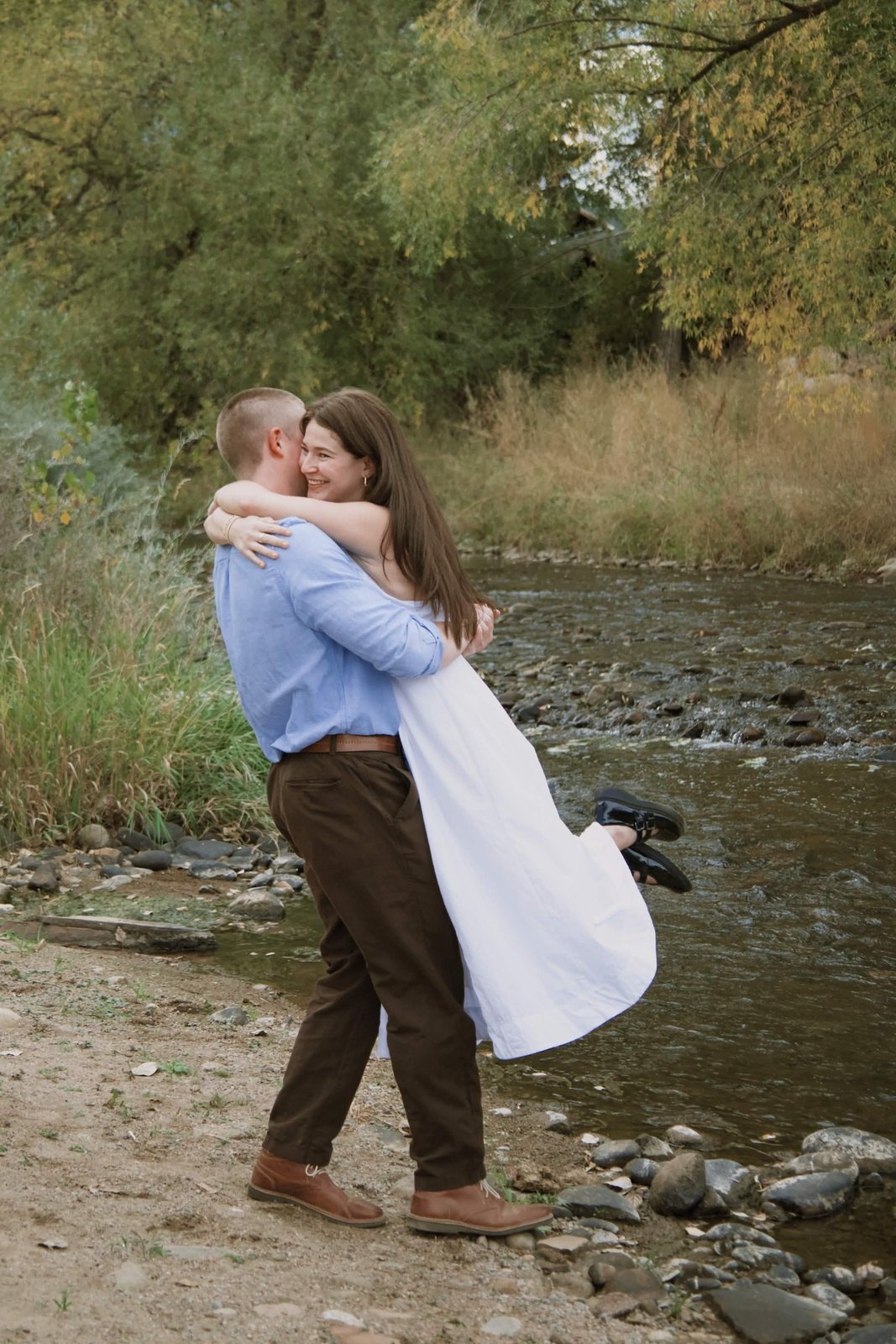 Couple laughing as he lifts her by a Colorado creek