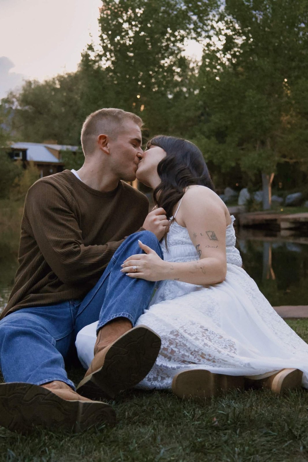 Couple kissing in the grass by the water at dusk