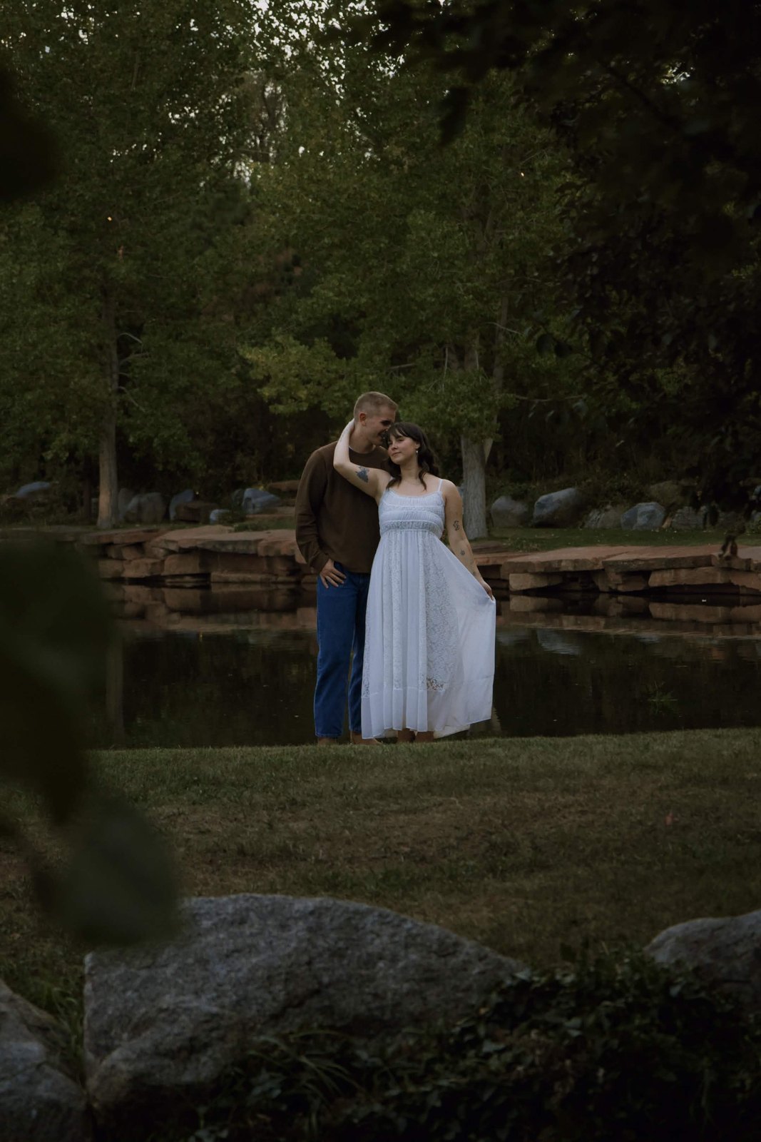 Couple by a pond at dusk framed by trees