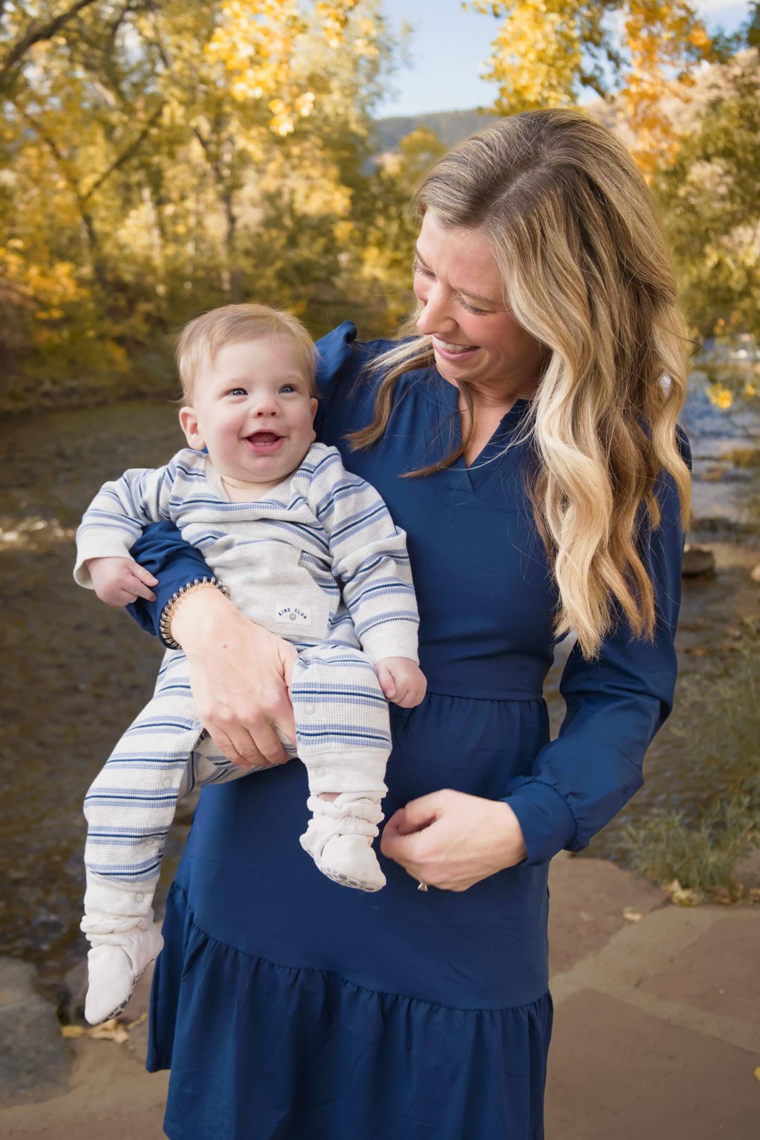 Mom holding her laughing baby by the river in fall